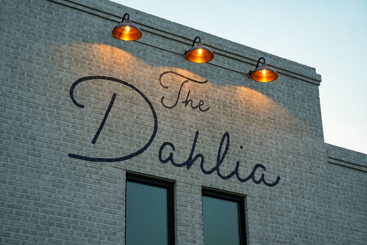 The Dahlia sign lit by gooseneck lamps on the brick building
